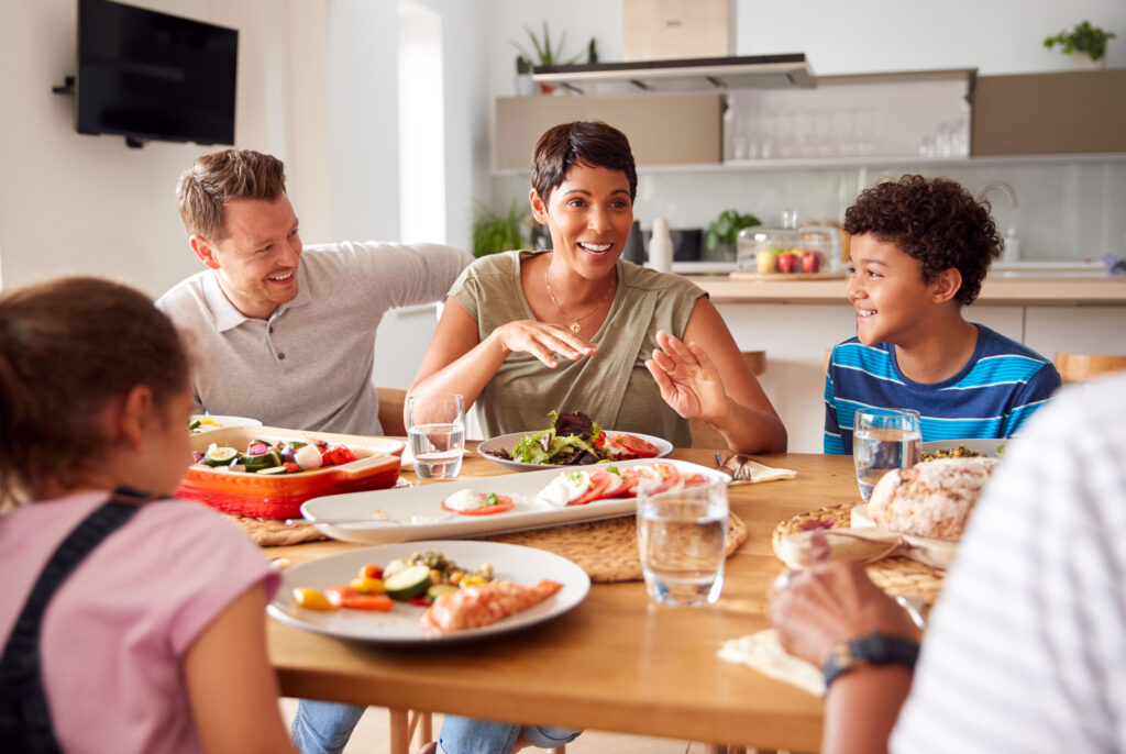Multi Generation Mixed Race Family Eating Meal Around Table At Home Together